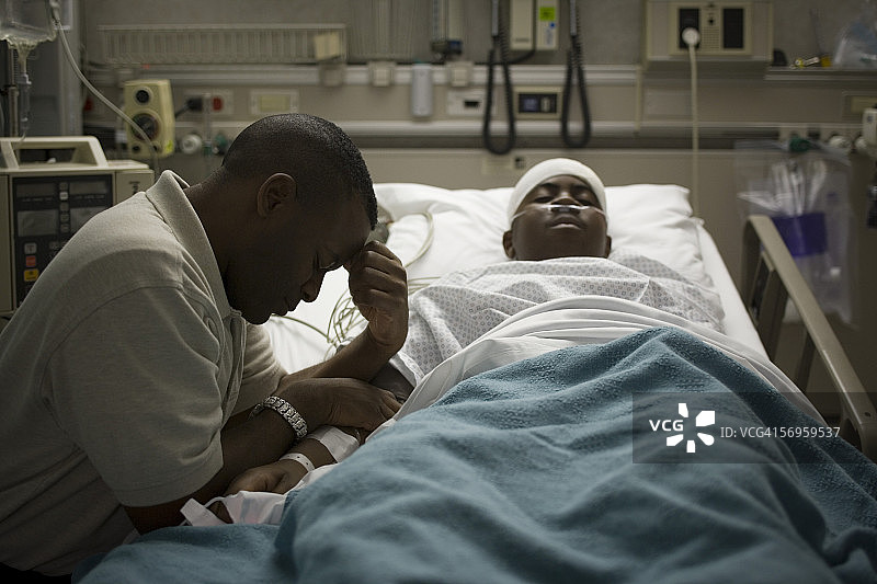 一个父亲坐在他儿子旁边的侧面躺在病床上图片素材