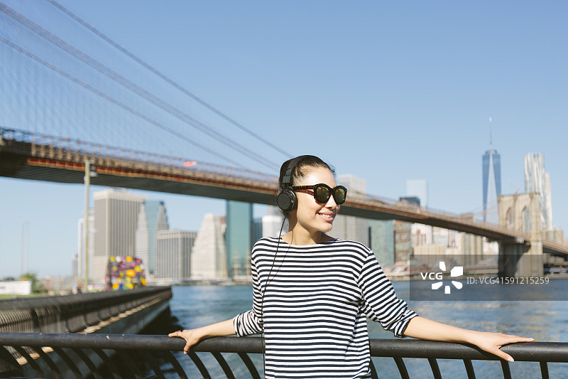 美国，纽约市，年轻女子在天际线前听耳机音乐的肖像图片素材