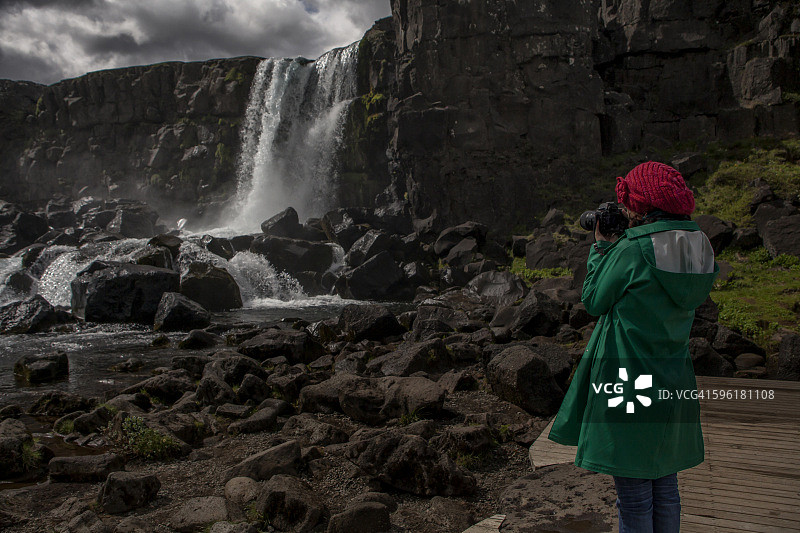 一名女子在Þingvellir国家公园以瀑布为背景图片素材
