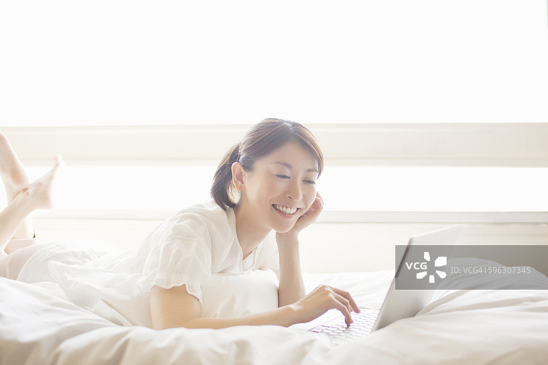 微笑的女人在床上使用笔记本电脑图片素材
