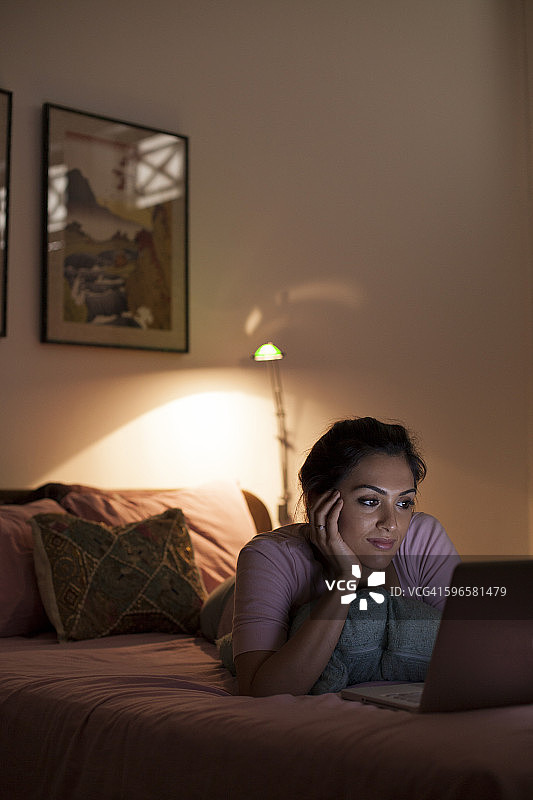 新加坡，一名年轻女子在床上用笔记本电脑放松图片素材