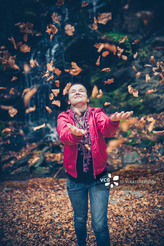 年轻女子在森林瀑布旁抛起秋叶图片素材