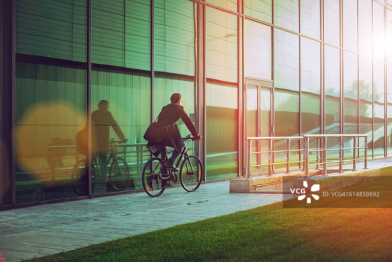 英俊的男人骑着自行车在现代化的办公楼旁边图片素材