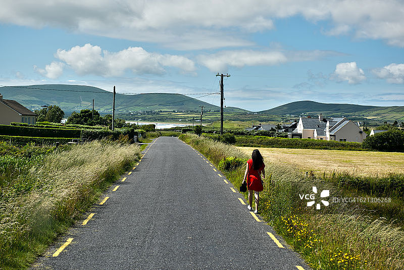 爱尔兰沃特维尔，一名身穿红色连衣裙的女子走在路边图片素材