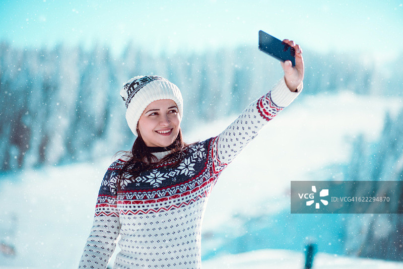 微笑的女孩享受冬天，在下雪的时候自拍图片素材