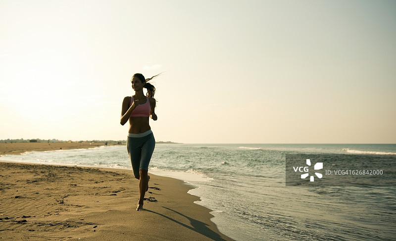 日出时，一个女人在岸上慢跑。图片素材