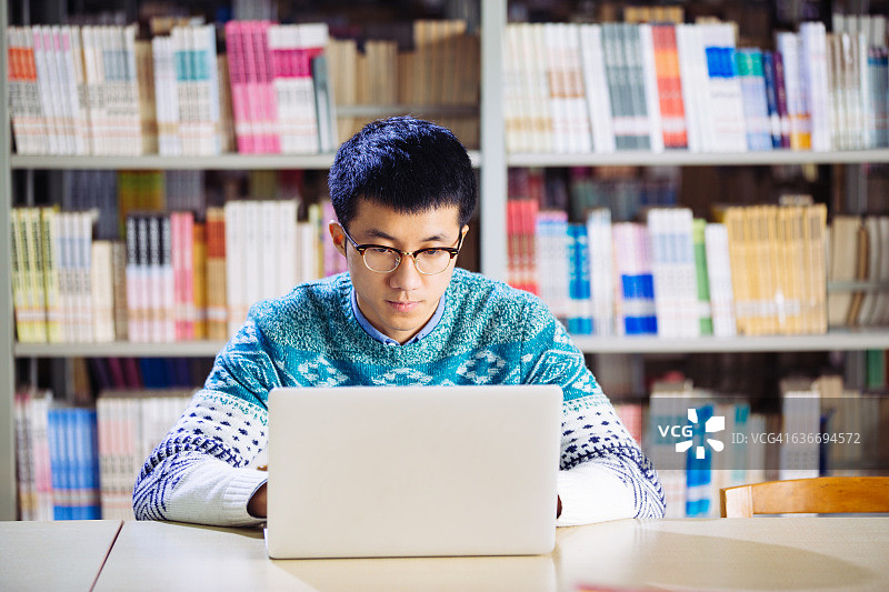 年轻的亚洲人在图书馆用笔记本电脑图片素材