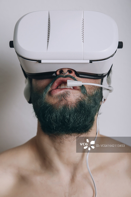 赤膊男子戴着虚拟现实眼镜和耳机咬他的嘴唇图片素材