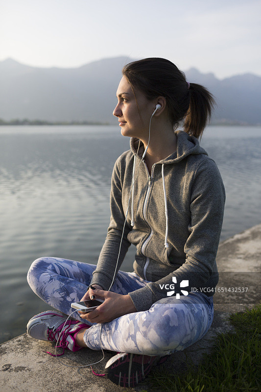 意大利莱科，年轻女子悠闲地坐在湖边听音乐图片素材