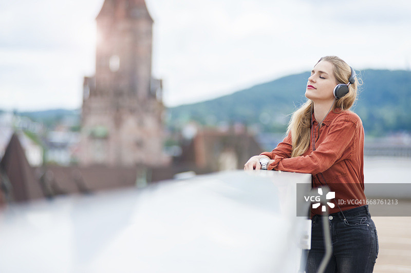 德国萨尔布吕肯，一名女子在屋顶露台上戴着耳机听音乐图片素材