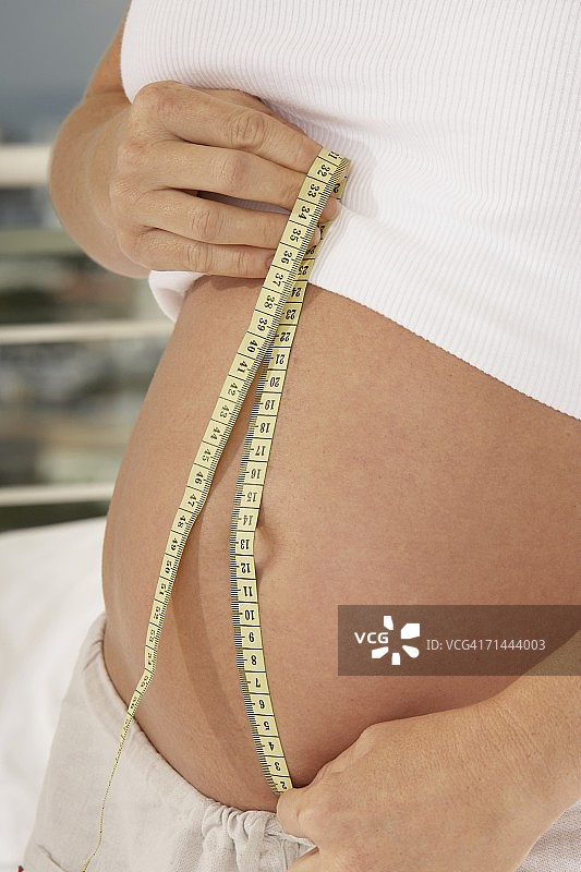 一个孕妇用卷尺测量她的腹部的中段视图图片素材
