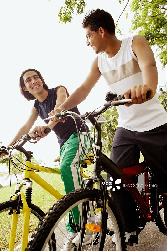 两个年轻人骑着自行车，低角度观看图片素材