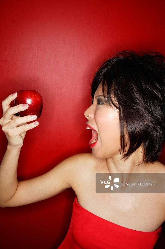 穿红管绳的女人拿着红苹果，嘴张着图片素材