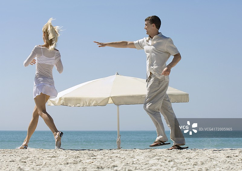 一对情侣在沙滩上绕着遮阳伞追逐图片素材