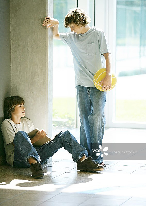 十几岁的男孩拿着篮球接近在走廊学习的第二个男孩图片素材
