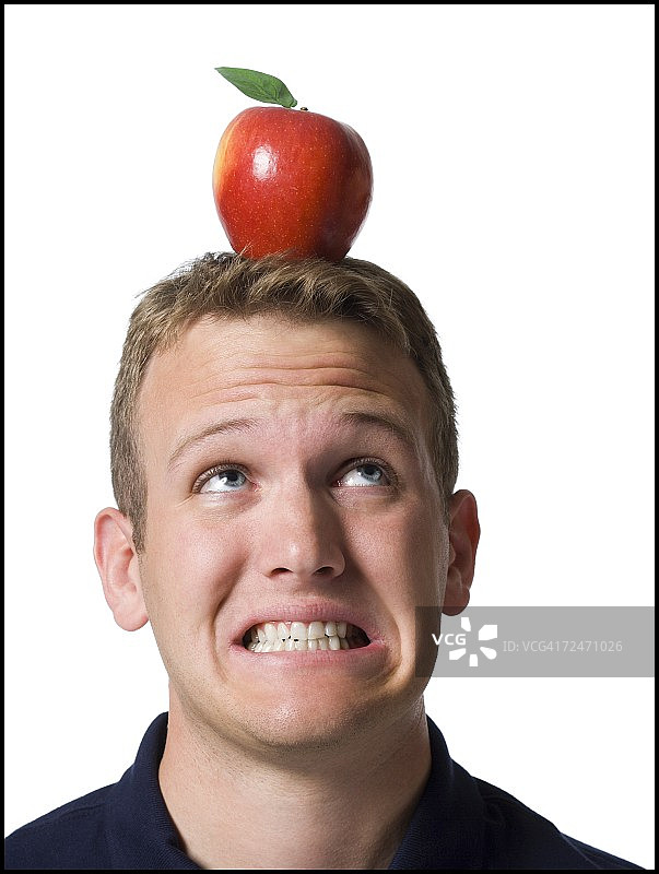一个年轻人的特写镜头，紧咬他的牙齿与苹果在他的头上图片素材