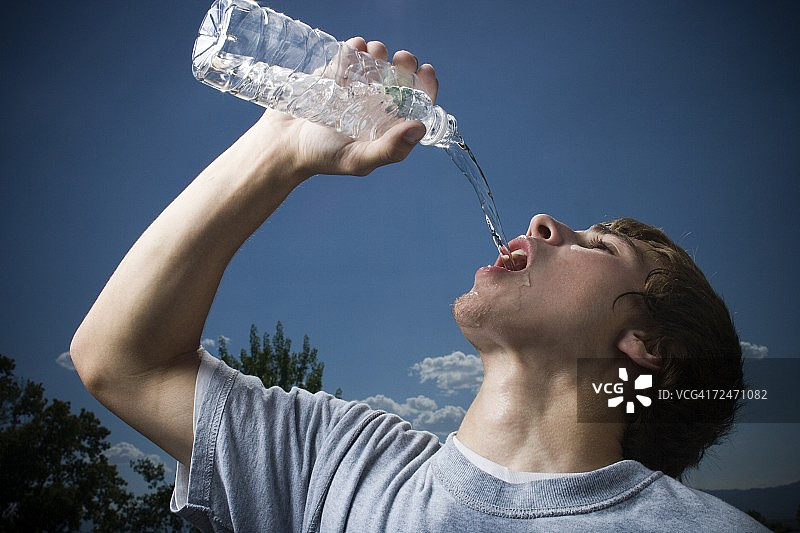 一个十几岁的男孩从一个水瓶里喝水的特写图片素材