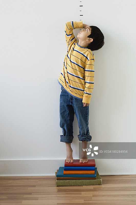 一个亚洲男孩站在身高标记前的书上图片素材