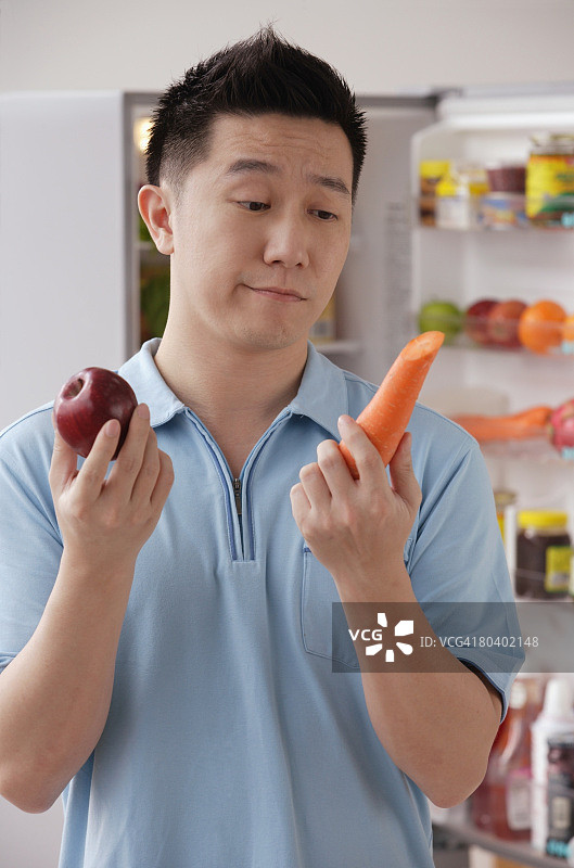 一个人拿着苹果和胡萝卜，看起来很沮丧图片素材