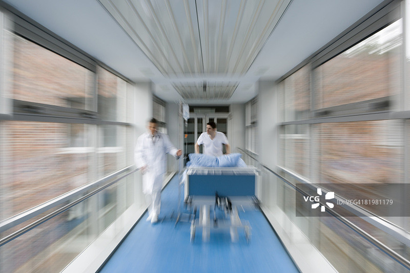 两名医护人员沿着走廊推着一张病床图片素材