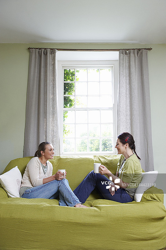 两个年轻女人坐在沙发上，拿着马克杯图片素材