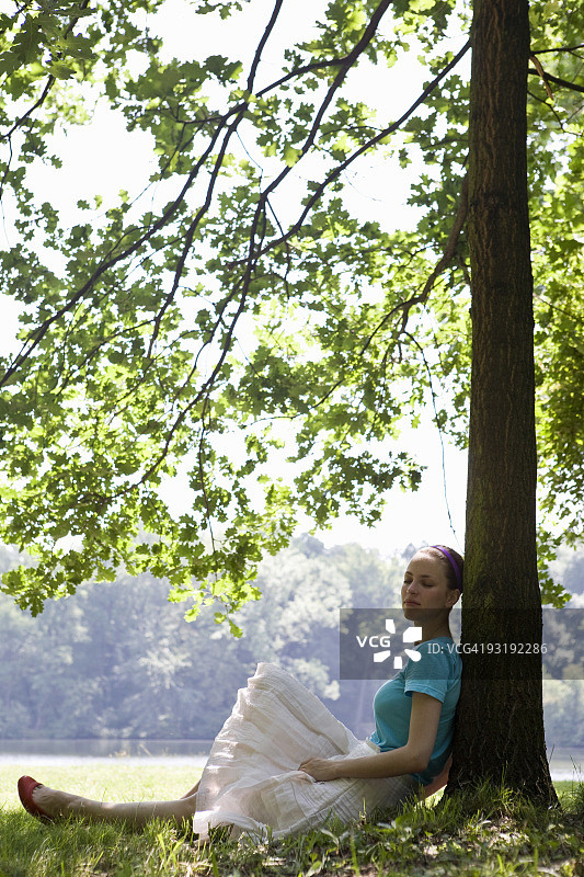 一个年轻女子靠在湖边的一棵树上图片素材