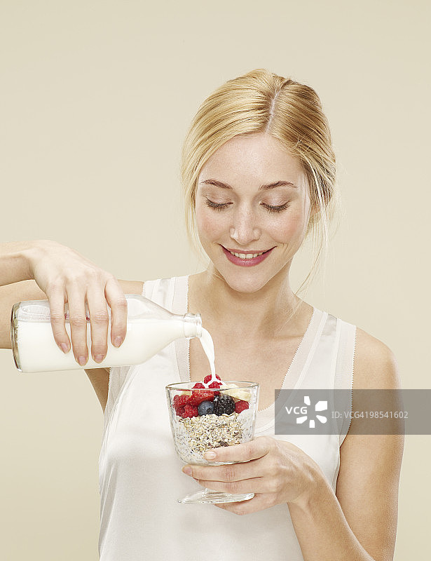 女人微笑着往麦片粥上倒牛奶图片素材