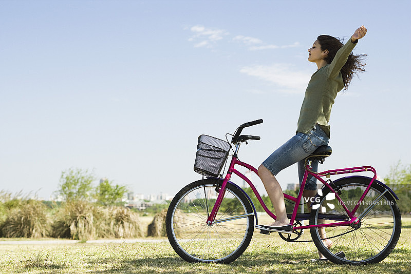 年轻女子坐在自行车上，双臂伸出，眼睛闭着图片素材