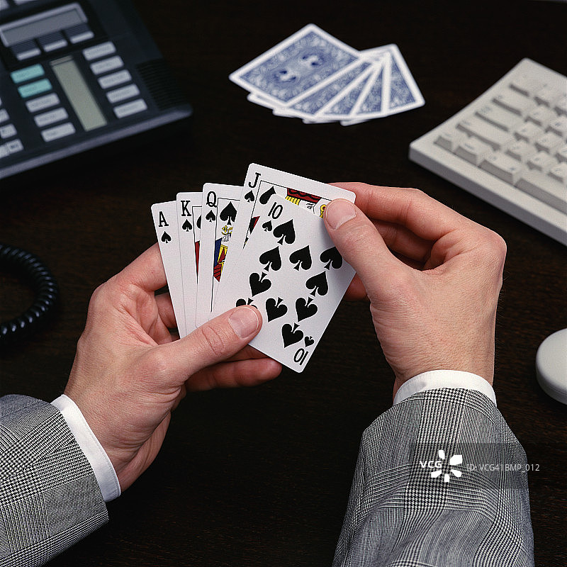 一个拿着扑克牌坐在桌子前的男人图片素材