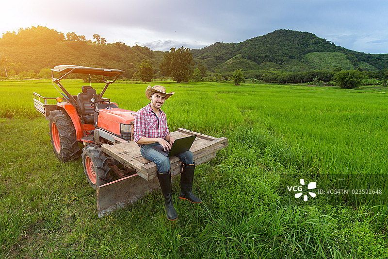 农民坐在拖拉机上记录生产力的增长，背景是稻田，山脉和天空。图片素材