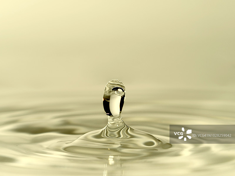 一组水滴悬在空中，落在水面上，形成图形和抽象形式，在一个彩色背景。图片素材