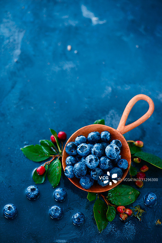蓝莓在手工木勺在夏天的雨在蓝色的背景与复制空间。小世界的概念。秋收美食摄影图片素材