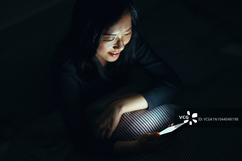 午夜黑暗中，年轻女子在床上使用智能手机图片素材