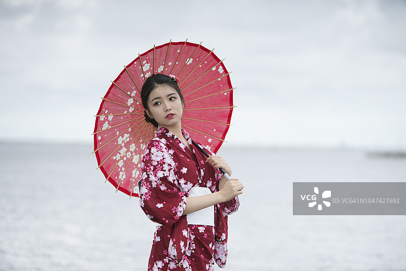 年轻的亚洲妇女的肖像穿着和服与红伞，走在海滩上图片素材