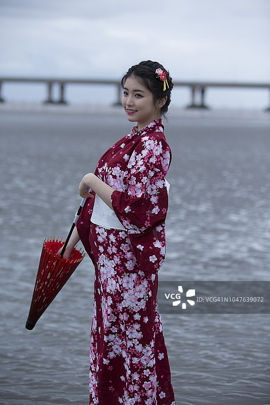 年轻的亚洲妇女的肖像穿着和服与红伞，走在海滩上图片素材