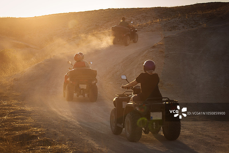 人们喜欢驾驶atv在卡帕多西亚山谷日落与许多灰尘的背景。图片素材