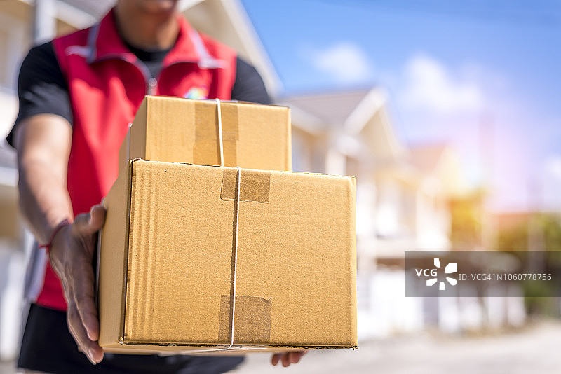 英俊的送货人在红色制服邮政交付盒子包装，快速和免费交付运输。网上购物和快递主题。图片素材