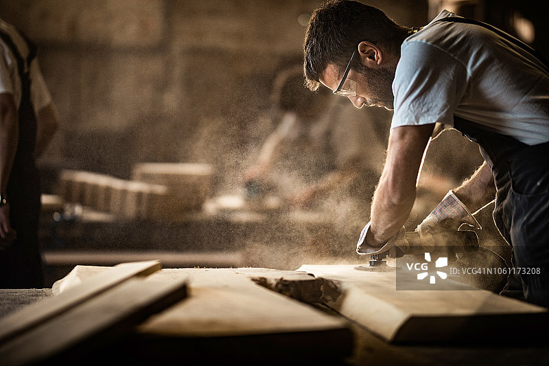 在一块木头上工作时用砂光机的年轻木匠。图片素材