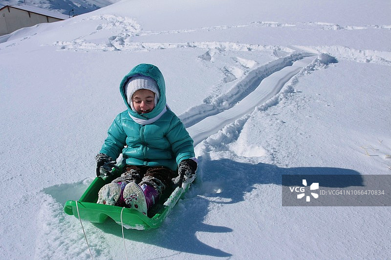 这个小女孩喜欢她的塑料雪橇，在雪地里很难骑，她发现了有趣的交通工具，冬季的罗马尼亚巴里尔湖图片素材