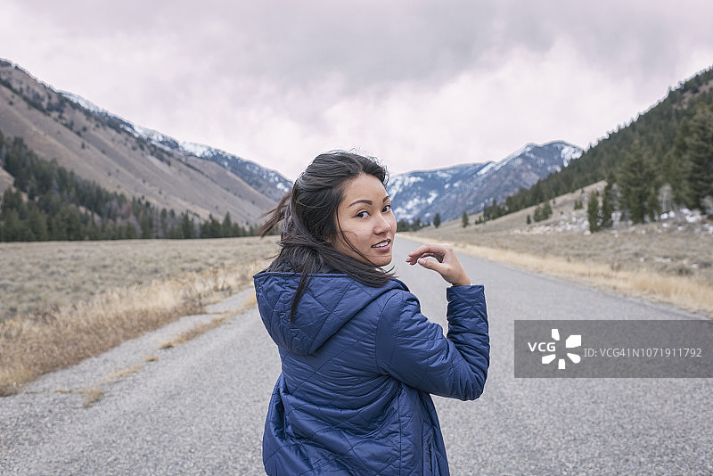 在寒冷的阴天，一个年轻女子走在山路上图片素材