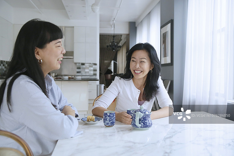在一间阁楼式的公寓里，两个亚洲女人一边享用零食和茶，一边谈笑风生。图片素材