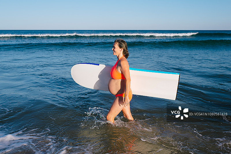 肖像成熟的孕妇与冲浪板在海滩图片素材