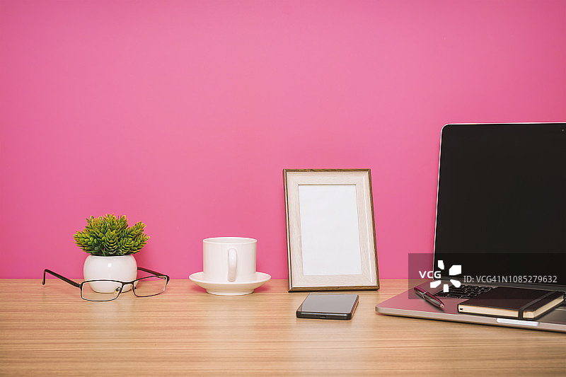 笔记本电脑，笔记本电脑，手机和咖啡杯放在粉红色背景的木桌上图片素材