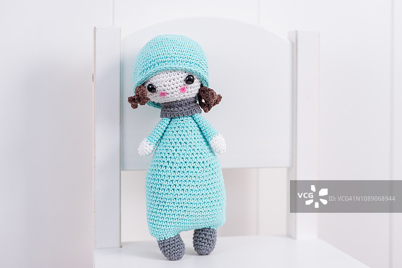 手工钩针娃娃在蓝色与围巾和帽子在一个白色的椅子上。图片素材