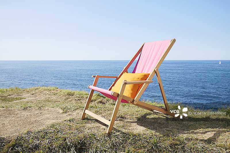在海边的草地上，蓝色的天空映衬着粉红色的靠背躺椅图片素材