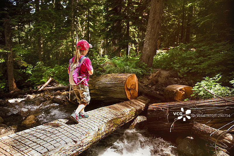 后视图的女孩与背包行走在步行桥上的河流在森林图片素材