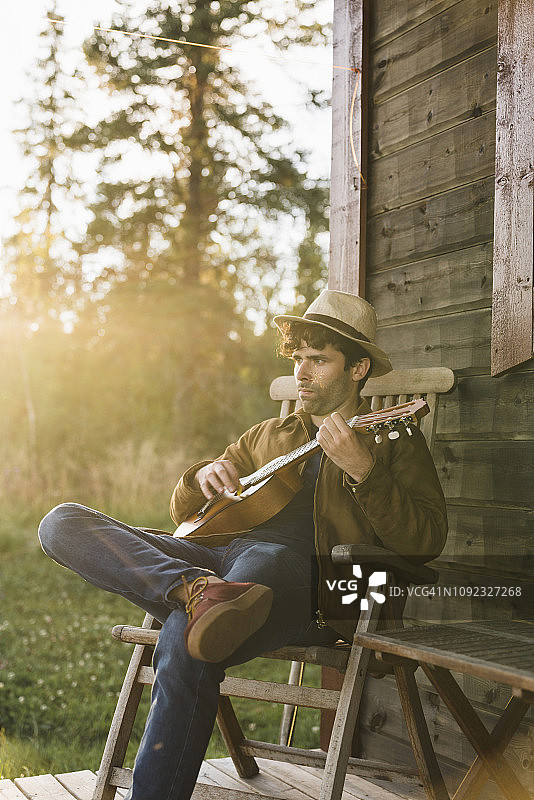 一个年轻人坐在木屋的阳台上，弹着四弦琴图片素材