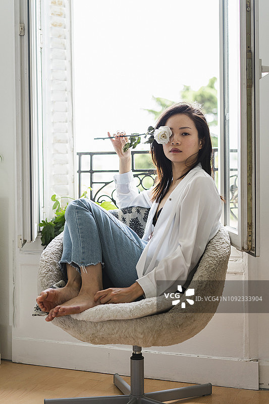 一幅迷人的年轻女子的画像，她坐在窗前，手捧白玫瑰图片素材