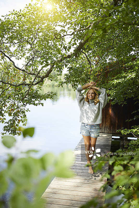 微笑的女人站在一个偏远的湖的木制码头上图片素材