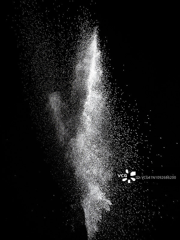一团白色的粉末颗粒在黑色的背景上碰撞而产生的爆炸。图片素材